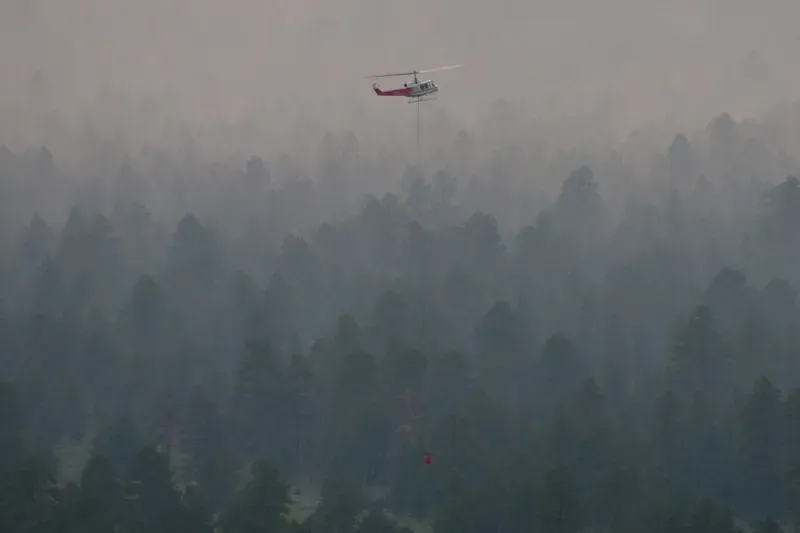 Helicopter carrying water through wildfire smoke over ponderosa pines