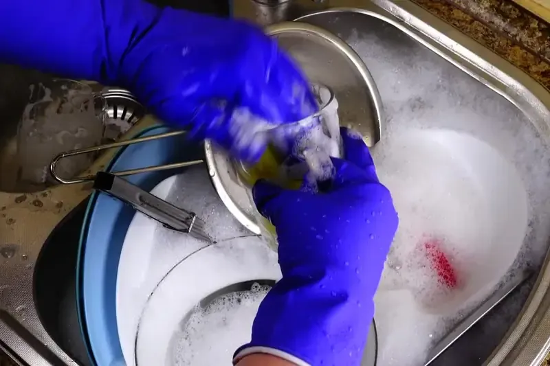 Gloved hands scrubbing a stainless sink